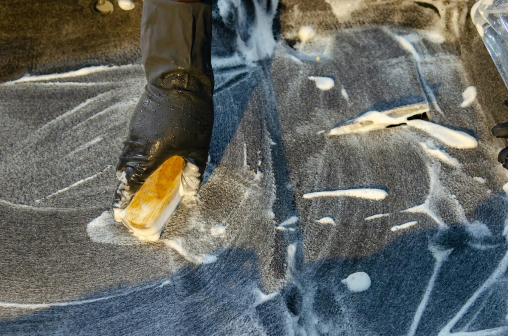 pexels-photo-5233260-5233260 A detailed view of cleaning in progress, focusing on a gloved hand using a brush with detergent on a surface.